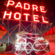 Padre sign on the rooftop at night with red glow and couple standing in front of them
