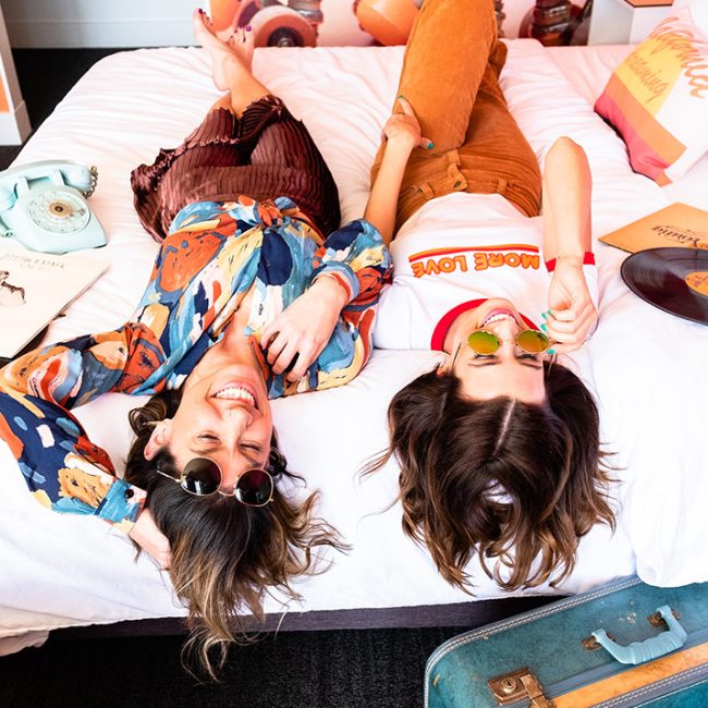 Two girls laying on a bed in Rambler Motel guest room