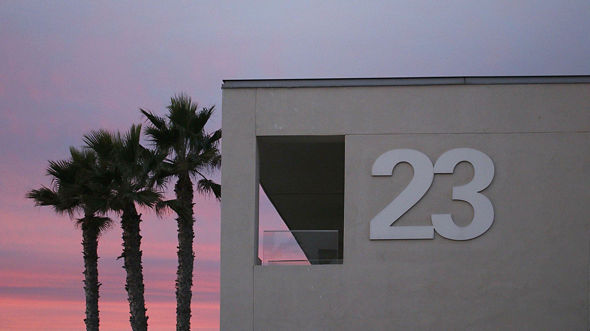 Purple and pink sunset with palm trees across the 23 sign on Tower23 Hotel